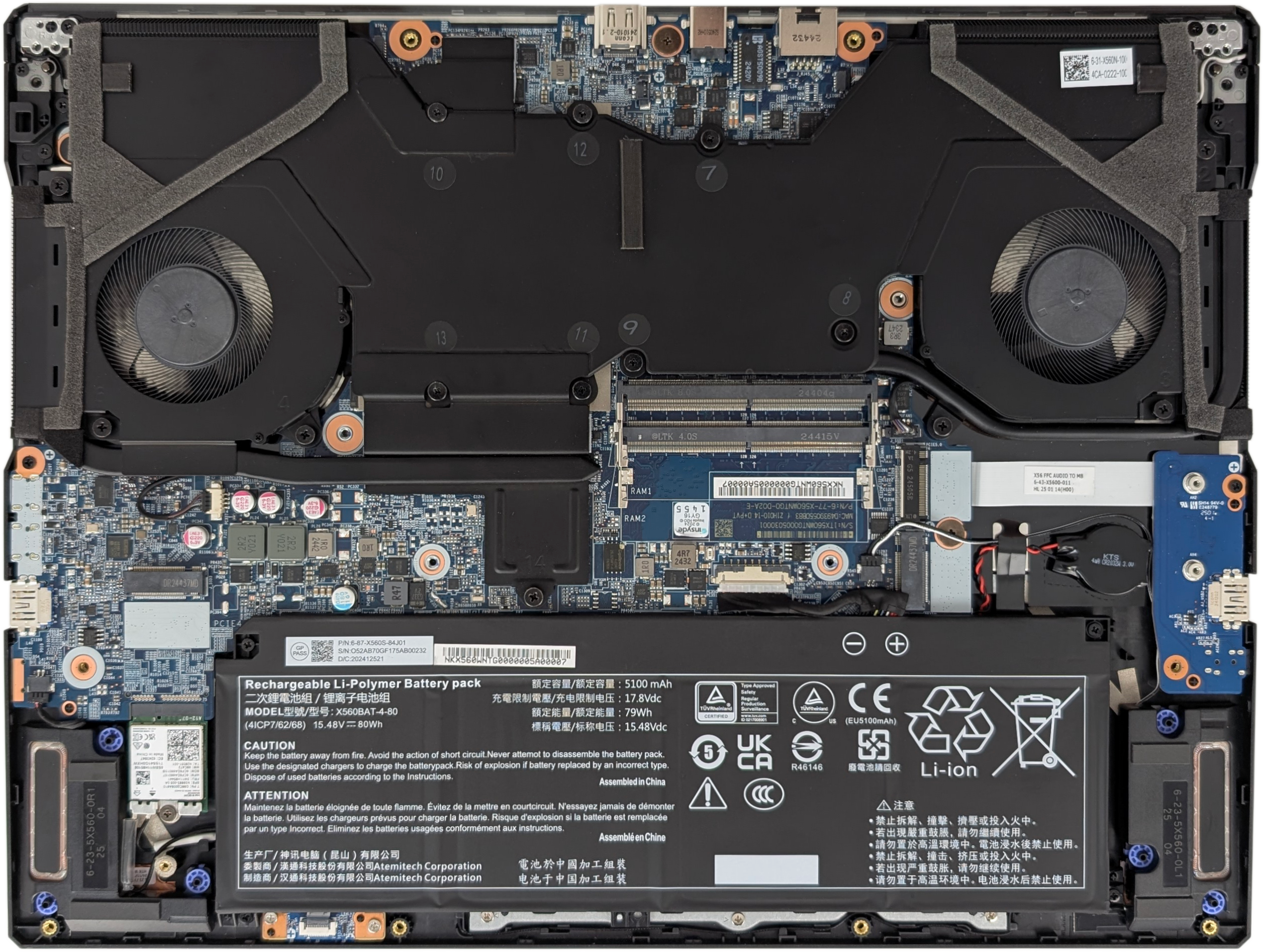 A picture of the internals of the Puget Mobile 16". The top half of the image is a solid-black heatsink, with two cooling fans about 40% the way down, on the far left and right sides. The (vertical) middle-third of the image is a blue PCB, with two SODIMM slots located in the middle (horizontally) of the area. Various other small components dot the PCB. Next to them, there are two M.2 slots. The lower third consists primarily of a black battery, which lists it as 80 WH. Next to the battery is a third M.2 slot.